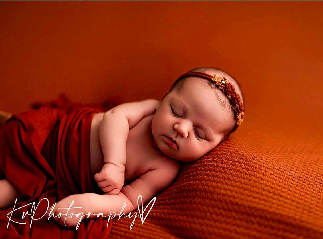 Naomi is registered to the contest to win money with this photo: baby, newborn, infant, sleeping, headband, blanket, knit_blanket, orange, warm_tone, portrait, studio, peaceful, wrapped, chubby_cheeks, closed_eyes, arm, pillow, cute, soft_texture, watermark