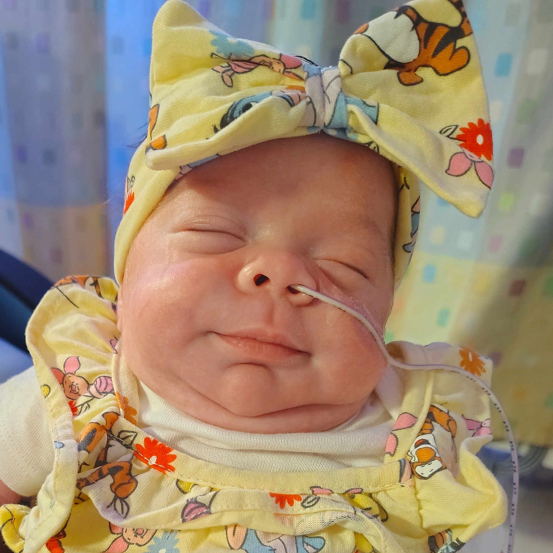 Iris Mae is registered to the contest to win money with this photo: baby, bow, chubby_cheeks, closed_eyes, cute, face, headband, indoors, infant, medical_tube, nasal_tube, newborn, patterned_clothing, person, portrait, sleeping, sleepy, smile, soft_lighting, yellow_clothing