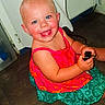 child, toddler, smiling, blue_eyes, dress, colorful_clothing, sitting, floor, indoor, plug, happy, cute, person, skin, face, short_hair, baby, holding_object, cheerful, rosy_cheeks