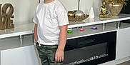Matthew is registered to the contest to win money with this photo: child, boy, smile, white_tshirt, camo_shorts, sneakers, indoor, floor, wooden_floor, cabinet, decor, golden_statue, vase, golden_foliage, love_sculpture, modern, furniture, happy, standing, casual