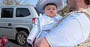 Remington is registered to the contest to win money with this photo: child, man, parking_lot, car, white_clothing, hat, vest, cap, outdoor, daytime, person, side_view, facial_expression, holding, vehicle, asphalt, tree, sky, casual_wear, footwear