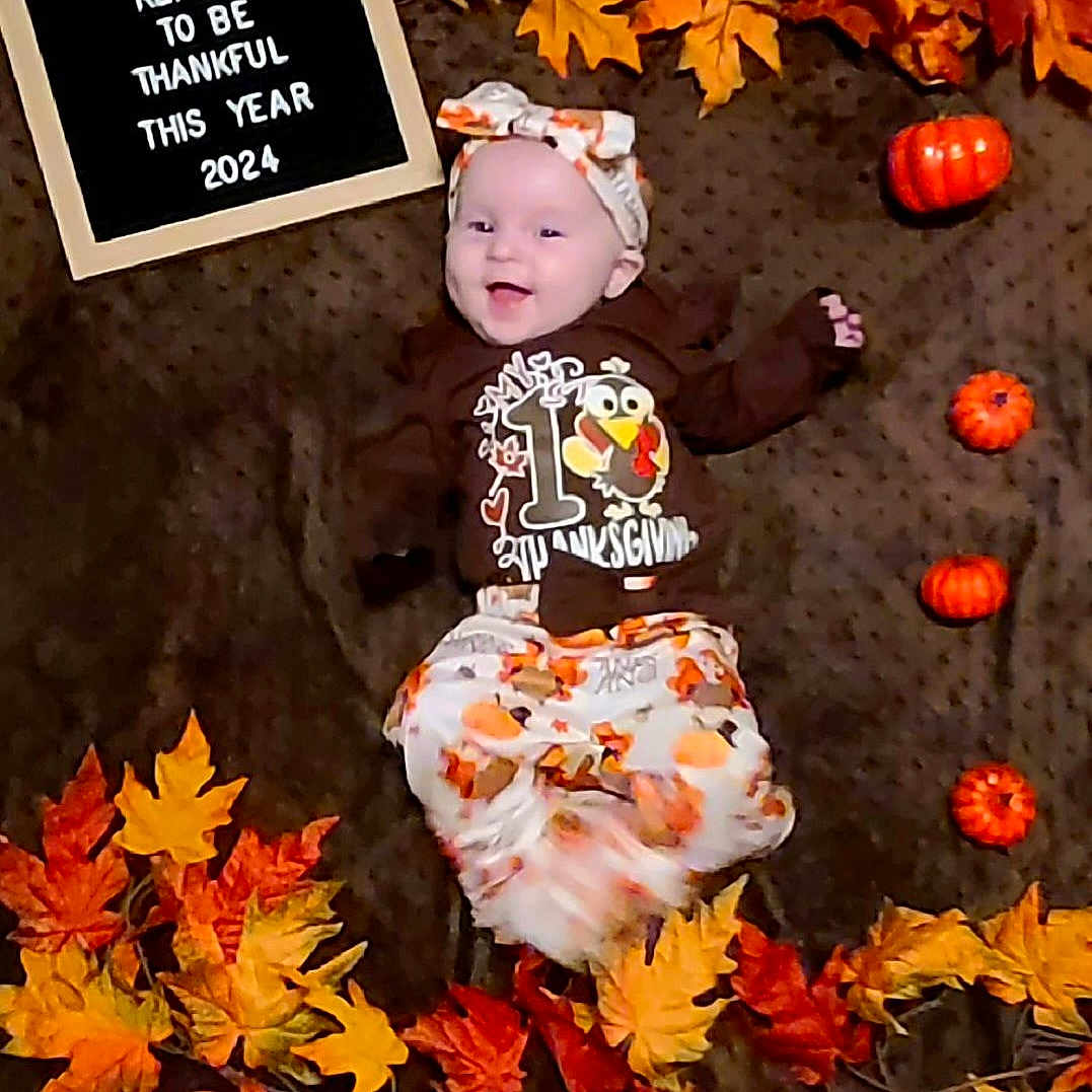 Novalynn is registered to the contest to win money with this photo: baby, clothing, dress, face, flower, food, head, leaf, maple, mapleleaf, person, petal, photography, plant, portrait, produce, sitting, squash, tree, vegetable