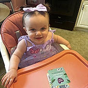 Lailah is registered to the contest to win money with this photo: baby, child, toddler, smiling, happy, portrait, high_chair, bow, headband, lavender_dress, butterfly, kitchen, indoor, tray, snack_package, home, furniture, seated, facial_expression, close_up