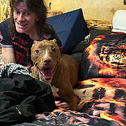 Sadie Jo is registered to the contest to win money with this photo: dog, person, bed, bedding, pillow, smile, indoor, happy, long_hair, black_shirt, red_shirt, couch, blanket, face, furniture, room, home, pet, brown_dog, casual