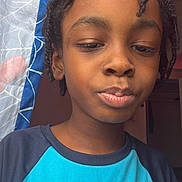 Devon is registered to the contest to win money with this photo: child, close_up, portrait, braided_hair, blue_shirt, curtain, indoor, person, face, expression, young, casual_clothing, looking_down, natural_light, home, curtain_pattern, head_and_shoulders, child_portrait, skin_tone, hair