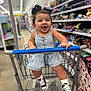 aisle, baby, black_bows, child, clothing, cute, fun, happy, indoor, infant, joyful, person, retail, romper, shopping, shopping_cart, smiling, sneakers, store, toddler