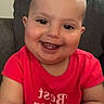 Remi is registered to the contest to win money with this photo: baby, child, smiling, red_shirt, text_on_clothing, indoor, couch, happy, portrait, person, cute, infant, sitting, face, head, skin, short_hair, young, toddler, bright_clothing