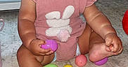 Remi joined the competition — help win amazing prizes! baby, child, pink_romper, bunny_design, plastic_eggs, carpet, indoor, cute, smiling, sitting, toy, playtime, floor, foot, hand, infant, young_child, face, person, home