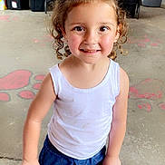 Luna is registered to the contest to win money with this photo: child, girl, bow, blue_bow, curly_hair, white_tank_top, denim_shorts, smiling, standing, indoor, store, snacks, table, person, casual_clothing, shoes, concrete_floor, red_wall, happy, cute