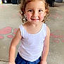 child, girl, bow, blue_bow, curly_hair, white_tank_top, denim_shorts, smiling, standing, indoor, store, snacks, table, person, casual_clothing, shoes, concrete_floor, red_wall, happy, cute