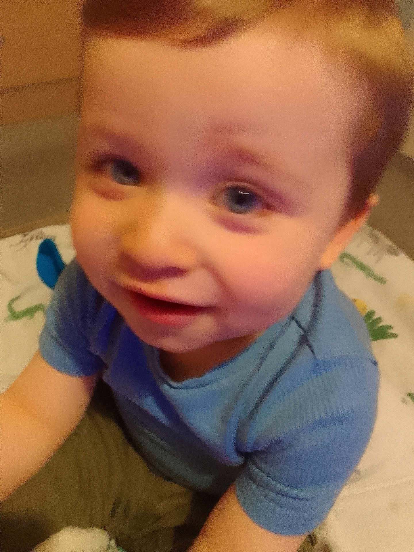 Jacob is registered to the contest to win money with this photo: child, toddler, blue_shirt, smiling, face, closeup, indoor, blanket, pattern, person, young_child, cute, happy, playful, baby, sitting, casual_clothing, portrait, young, blurry