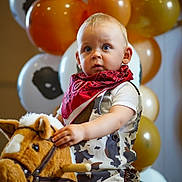 Dexter is registered to the contest to win money with this photo: child, toddler, toy_horse, plush_toy, balloons, cowboy_outfit, bandana, indoor, party, celebration, cute, portrait, young_child, costume, festive, playful, person, face, blue_eyes, light