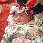 Eline a rejoint le concours — aidez-le/la à gagner de superbes lots ! baby, black, blanket, bonnet, button, chain, child, clothing, cozy, cute, face, infant, knitted_sweater, lace, orange, portrait, purple_hat, resting, sleeping, smiling