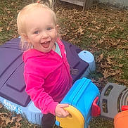 Emilia is registered to the contest to win money with this photo: child, toddler, girl, smiling, outdoors, backyard, playset, toy, pink_jacket, ponytail, happy, grass, leaves, plastic_toy, candid, shoes, expression, portrait, fun, playing