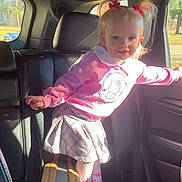 Emilia is registered to the contest to win money with this photo: arm, backpack, car_interior, child, girl, hair_bows, hello_kitty, knee_socks, pigtails, pink_sweater, playful_pose, portrait, rear_seat, seat, skirt, smile, sneakers, sunlight, toddler, window