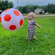 Emilia is registered to the contest to win money with this photo: toddler, child, grass, outdoor, play, barefoot, striped_dress, inflatable_ball, soccer_ball, greenery, sky, cloudy, trees, house, smiling, happy, person, nature, fun, daytime