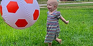 Emilia is registered to the contest to win money with this photo: barefoot, child, cloudy, daytime, fun, grass, greenery, happy, house, inflatable_ball, nature, outdoor, person, play, sky, smiling, soccer_ball, striped_dress, toddler, trees