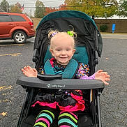Emilia is registered to the contest to win money with this photo: toddler, stroller, child, smile, colorful_clothing, striped_leggings, autumn, fall_foliage, parking_lot, car, tree, outdoor, hair_ties, babytrend_stroller, happy, playful, pigtails, pavement, person, daytime