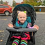 toddler, stroller, child, smile, colorful_clothing, striped_leggings, autumn, fall_foliage, parking_lot, car, tree, outdoor, hair_ties, babytrend_stroller, happy, playful, pigtails, pavement, person, daytime
