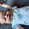 Colt is registered to the contest to win money with this photo: baby, newborn, child, infant, portrait, lying_down, blanket, gray_blanket, onesie, clothing, stitch_character, cartoon_print, face, eyes_open, hair, arm, hand, indoor, cozy, photography