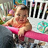 Ember is registered to the contest to win money with this photo: baby, crib, toy, pink_foam_bar, smiling, child, indoor, stuffed_animal, blanket, colorful, playroom, clothing, face, hand, person, furniture, cute, happy, portrait, infant