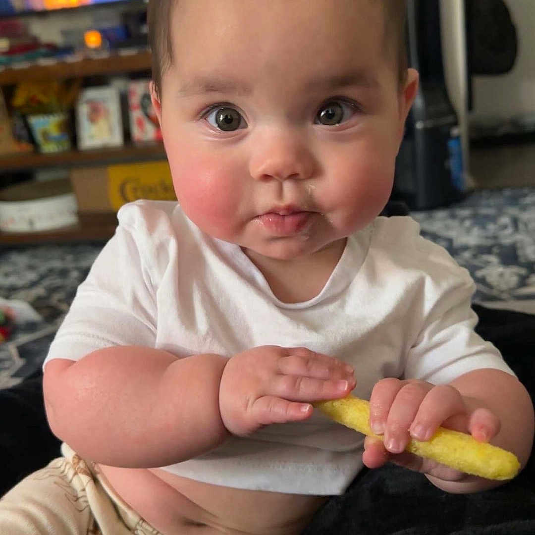 Ember joined the competition — help win amazing prizes! baby, child, infant, white_shirt, pants, toy, snack, indoor, carpet, furniture, face, hands, curious, sitting, home, cute, person, young, chubby, expression