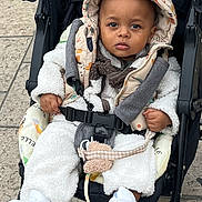 Nayem participe au concours pour gagner de l'argent avec cette photo : toddler, child, stroller, hooded_vest, white_shoes, outdoor, pavement, baby_clothes, straps, serious_expression, seatbelt, cute, warm_clothing, baby, person, portrait, casual, walking, urban, daytime