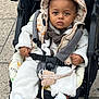 toddler, child, stroller, hooded_vest, white_shoes, outdoor, pavement, baby_clothes, straps, serious_expression, seatbelt, cute, warm_clothing, baby, person, portrait, casual, walking, urban, daytime
