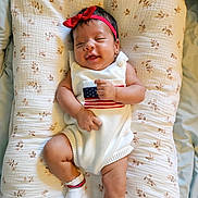 Kaveri joined the competition — help win amazing prizes! baby, infant, child, portrait, lying_down, smiling, red_headband, bow, white_outfit, striped_clothing, socks, floral_blanket, cushion, bed, indoors, close_up, cute, happy, relaxed, photography