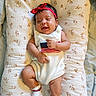 baby, infant, child, portrait, lying_down, smiling, red_headband, bow, white_outfit, striped_clothing, socks, floral_blanket, cushion, bed, indoors, close_up, cute, happy, relaxed, photography