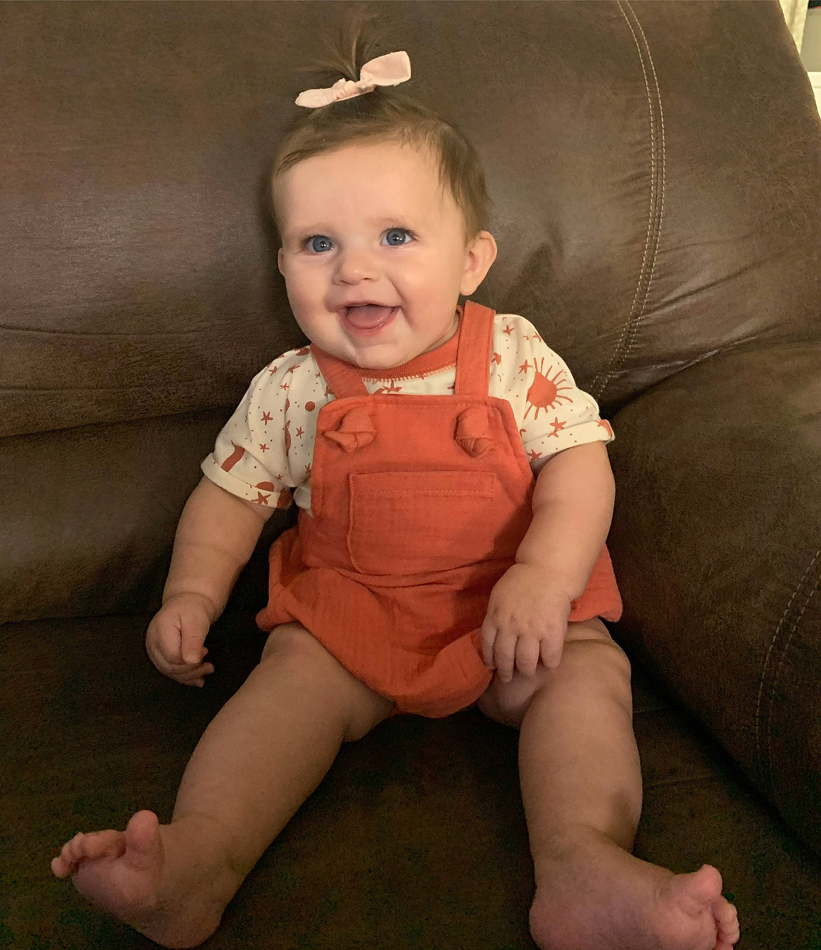 Norah joined the competition — help win amazing prizes! baby, baby_toddler_clothing, cheek, child, comfort, couch, eye, finger, hair, happy, head, human_body, human_leg, person, sitting, skin, sleeve, smile, thigh, thumb