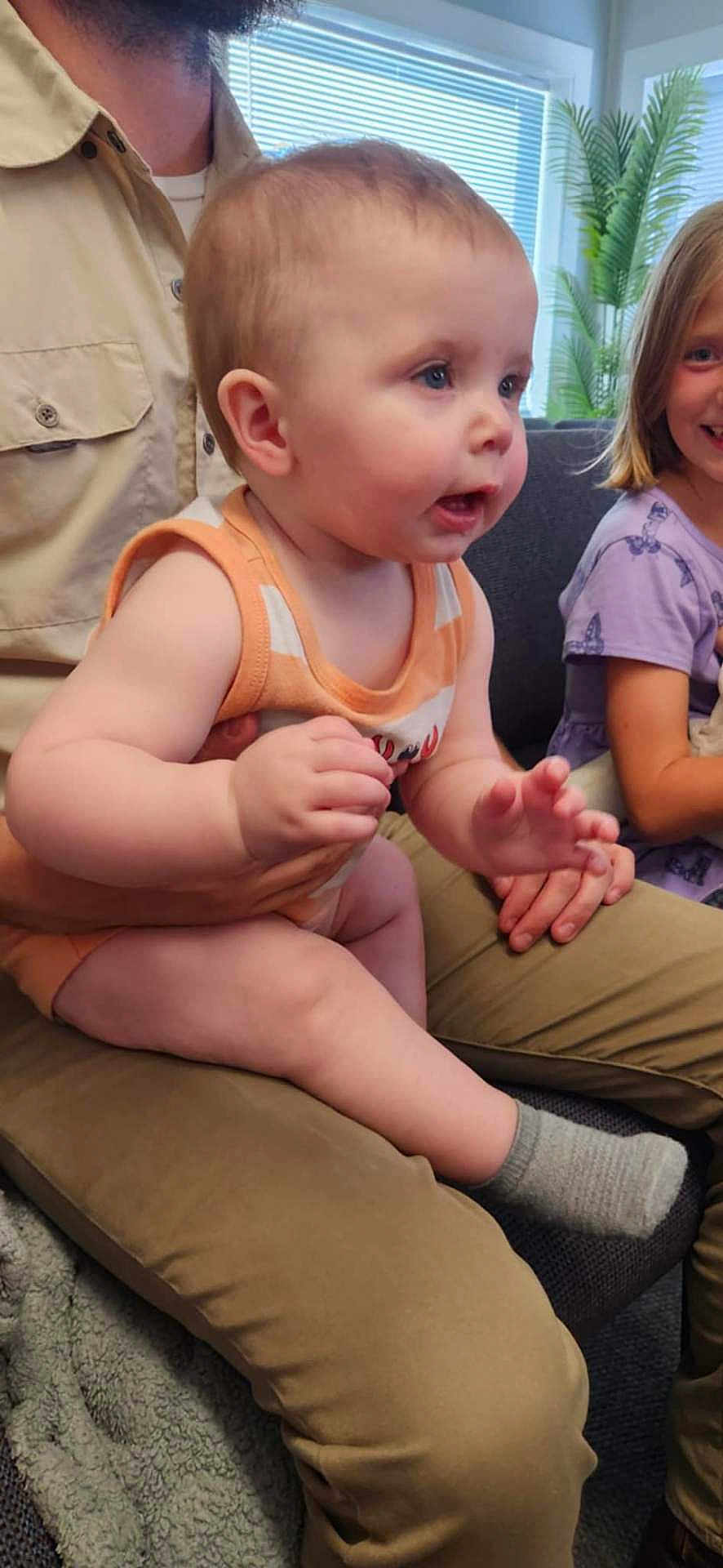 Algan joined the competition — help win amazing prizes! baby, child, adult, person, smiling, tank_top, purple_dress, butterfly_print, living_room, window, plant, couch, blanket, socks, legs, hands, face, curious, seated, family