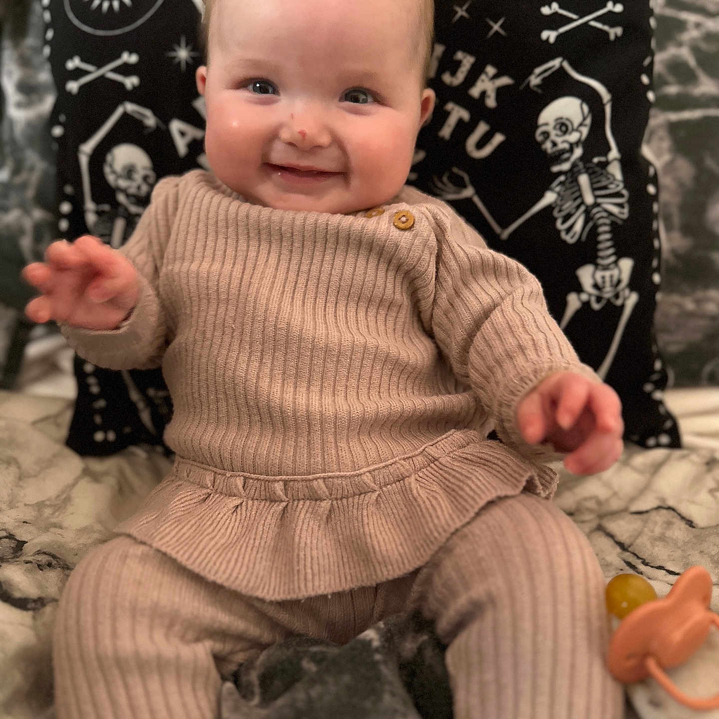 Frances joined the competition — help win amazing prizes! baby, beige_outfit, blanket, celestial_symbols, child, cozy, cute, face, hand, happy, indoor, infant, pacifier, pillow, portrait, ribbed_clothing, seated, skeleton_design, smiling, soft_fabric