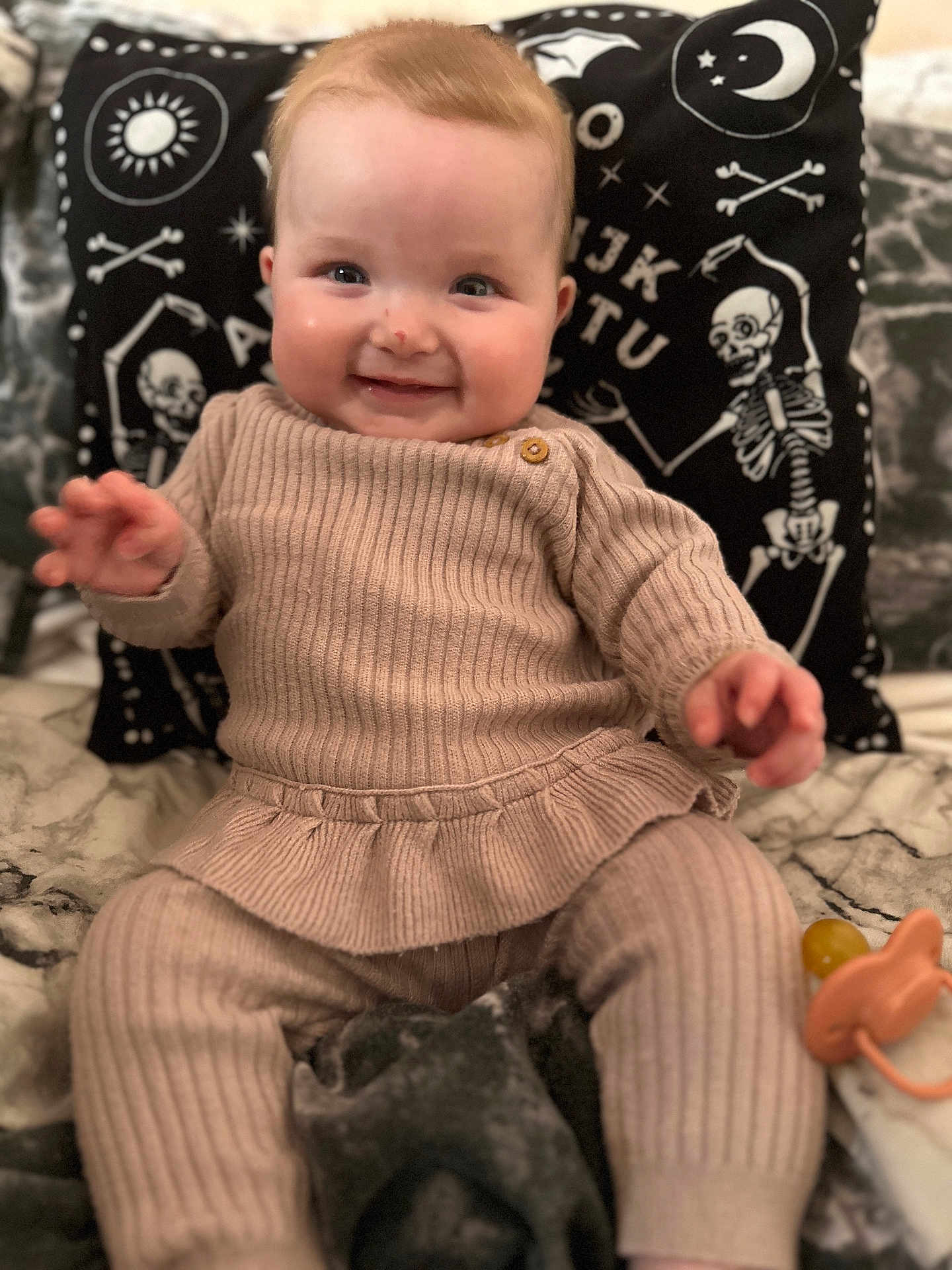Frances joined the competition — help win amazing prizes! baby, child, smiling, ribbed_clothing, beige_outfit, blanket, pacifier, pillow, skeleton_design, celestial_symbols, indoor, portrait, happy, seated, cute, infant, face, hand, cozy, soft_fabric