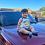 blue_sky, car, casual_clothing, child, daytime, face, hair, hood, outdoor, person, pikachu, reflection, shorts, smiling, socks, suburban, sunlight, tank_top, toddler, vehicle