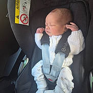George is registered to the contest to win money with this photo: baby, newborn, car_seat, infant, child, white_clothing, knitwear, sleeping, car_interior, seatbelt, safety, cute, small_hands, patterned_pants, footwear, resting, peaceful, seat, child_safety, portrait