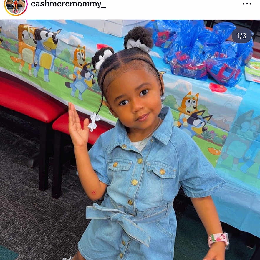 Truly is registered to the contest to win money with this photo: toddler, child, denim_dress, socks, shoes, party, table, gift_bags, cartoon_characters, hair_buns, playful_pose, indoor, carpet, red_chair, smiling, person, cute, fashion, young_child, happy