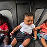 child, toddler, car_seat, seatbelt, smiling, curious, clothing, red_shirt, white_shirt, denim_skirt, hair_accessories, indoors, transportation, seat, cute, people, portrait, sitting, baby, friendship