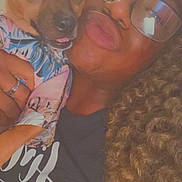 Ace is registered to the contest to win money with this photo: person, dog, glasses, curly_hair, puckered_lips, indoor, close_up, holding, clothing, cute, small_dog, portrait, warm_lighting, face, casual, affection, expression, human, animal, friendship