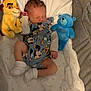 baby, newborn, sleeping, mickey_mouse, onesie, plush_toy, lion_toy, blue_bear, blanket, sock, infant, bed, resting, cute, soft, child, cozy, indoors, comfort, peaceful