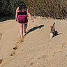 person, cat, sand, footprints, nature, outdoor, walking, bushes, barefoot, collar, sunlight, summer, animal, pet, back_view, path, daytime, casual, relaxation, adventure