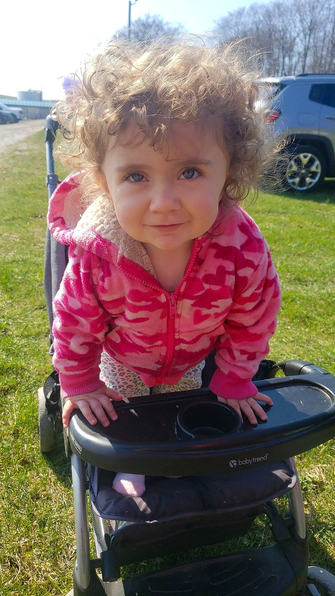 Hailey is registered to the contest to win money with this photo: automotive_tire, baby_toddler_clothing, car, child, face, family_car, fun, grass, lawn, magenta, people_in_nature, person, plant, recreation, sitting, smile, spring, tire, toddler, vehicle