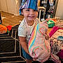 toddler, child, smiling, indoor, hat, pillow, rainbow, toy, rug, floor, furniture, blanket, clothing, socks, playroom, happy, face, person, home, cute