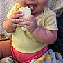 baby, child, smiling, eating, bread, blanket, yellow_clothing, pink_clothing, happy, indoor, cute, infant, person, face, hands, seated, cozy, soft_texture, closeup, portrait
