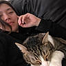 cat, tabby_cat, white_paws, sleeping, person, face, portrait, selfie, couch, indoor, home, relaxing, dark_clothing, hand, closeup, pet, furry, whiskers, cozy, casual