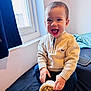 toddler, child, smiling, happy, indoors, bed, window, sweater, pants, shoe, footprints, hand, face, person, curtain, light, home, cozy, cute, playful