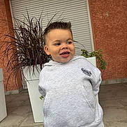 évan a rejoint le concours — aidez-le/la à gagner de superbes lots ! child, boy, hoodie, smiling, outdoor, plant, planter, tiled_floor, short_hair, casual_clothing, nike, playful, young, portrait, standing, expression, white_planter, orange_wall, background, daylight