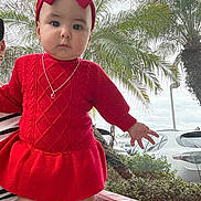Daireliz is registered to the contest to win money with this photo: baby, infant, child, red_dress, large_bow, necklace, outdoor, palm_trees, parking_lot, car, portrait, sitting, red_chair, cute, serious_expression, fashion, earrings, hand, plants, daytime