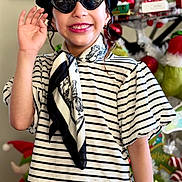 Samantha is registered to the contest to win money with this photo: child, smiling, beret, sunglasses, striped_shirt, scarf, holiday_decorations, grinch, christmas, festive, indoors, portrait, hand_wave, happy, fashion, accessories, toy, decor, person, cute