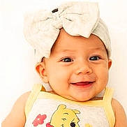 Emily is registered to the contest to win money with this photo: baby, child, smiling, headband, bow, yellow_clothing, cartoon_character, face, portrait, happy, cute, infant, closeup, light_background, cheerful, young_child, apparel, person, indoors, headwear